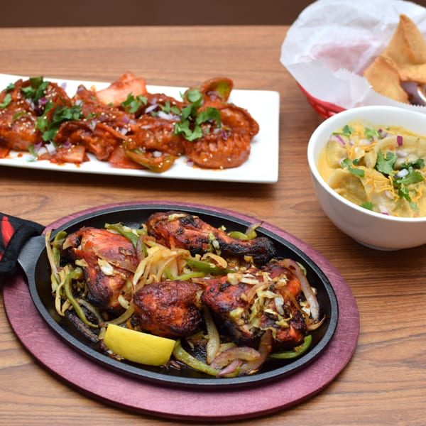 Indian dishes: sizzling tandoori chicken, chili momos, and a bowl of momo soup with chips.