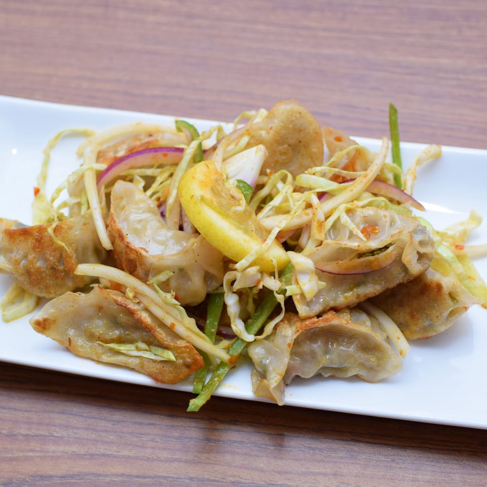 Fried dumplings with shredded cabbage, red onion, green peppers, and a lemon wedge on a white plate.