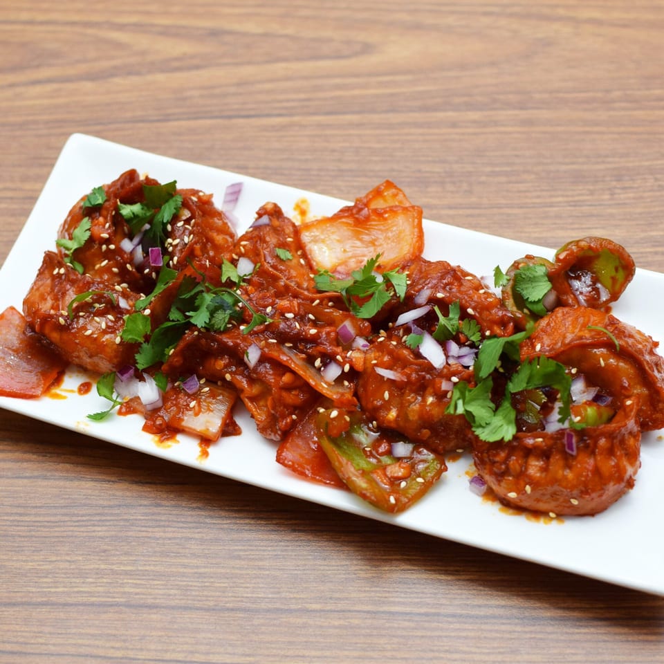 Indian chili momos, garnished with cilantro, sesame seeds, and chopped red onions on a white plate.