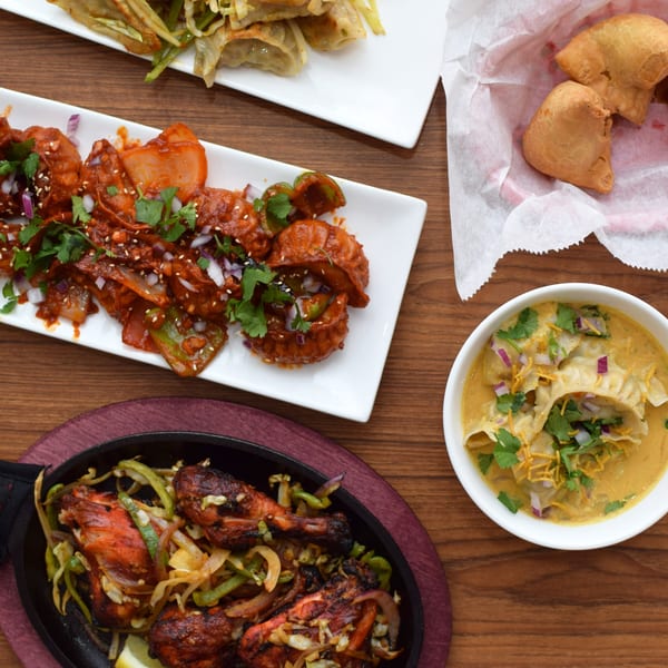 A top-down view of various Indian dishes, including momos, tandoori chicken, and samosas.