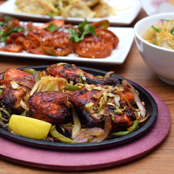 Sizzling Indian tandoori chicken with onions, peppers, and a lemon wedge on a cast iron plate.