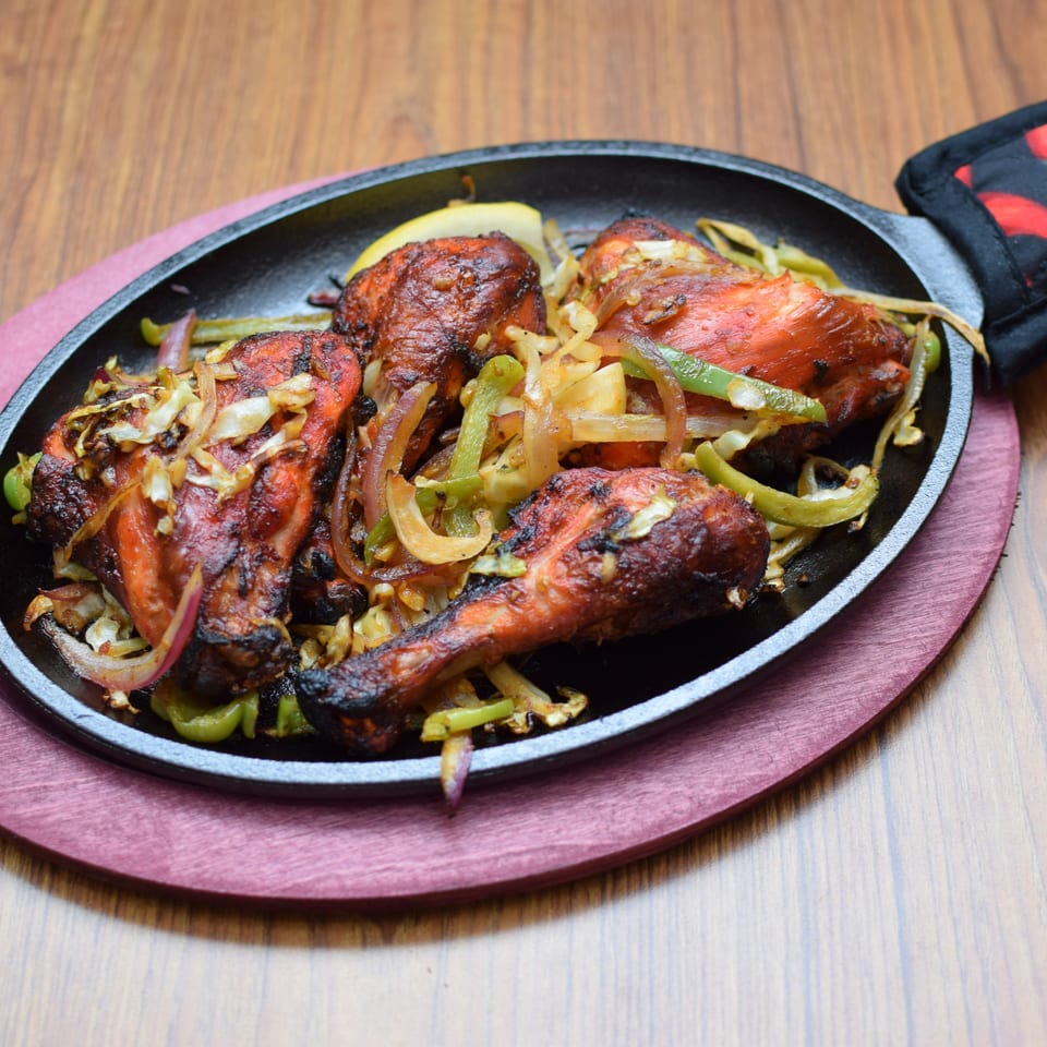 Sizzling Indian tandoori chicken with onions and bell peppers on a black cast iron platter.