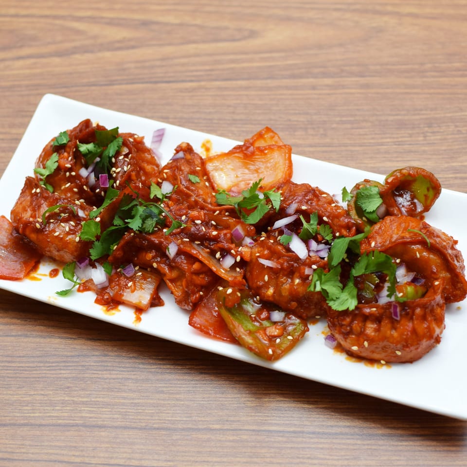 Spicy Indian momos with red sauce, cilantro, sesame seeds, and chopped onions on a white plate.