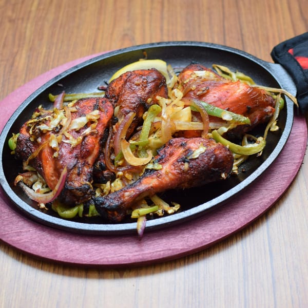 Indian tandoori chicken drumsticks with sautéed onions and green peppers on a sizzling platter.
